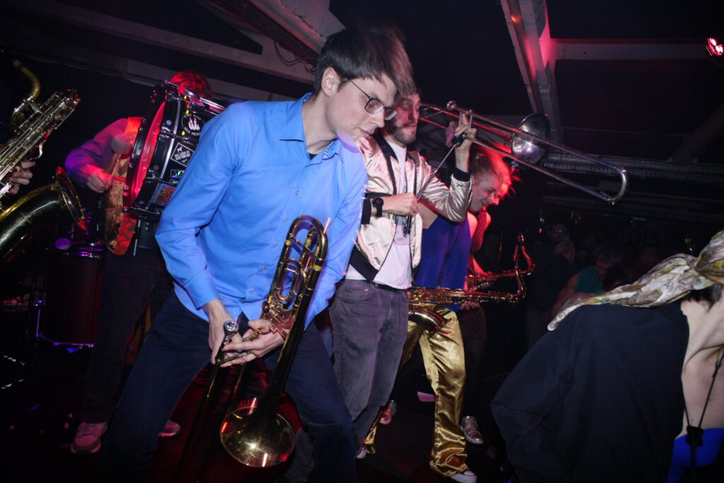 Photograph of a brass band playing and dancing on a stage
