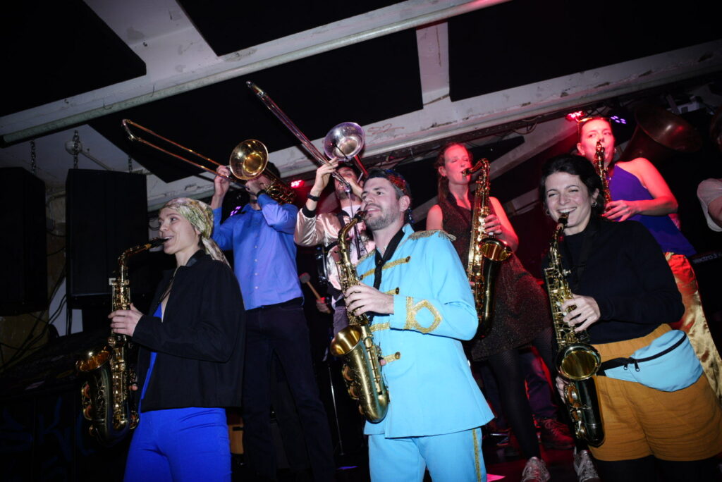 Photograph of a brass band playing on a stage at a club concert